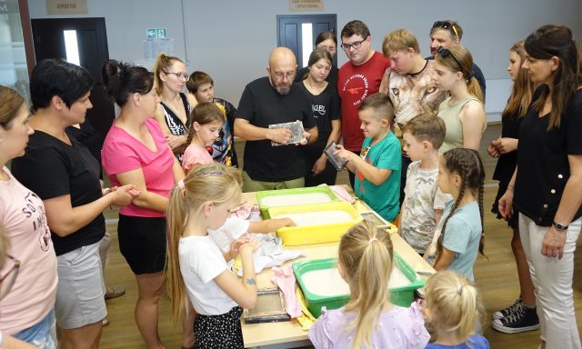 mężczyzna tłumaczy uczestnikom warsztatów metodę robienia papieru czerpanego