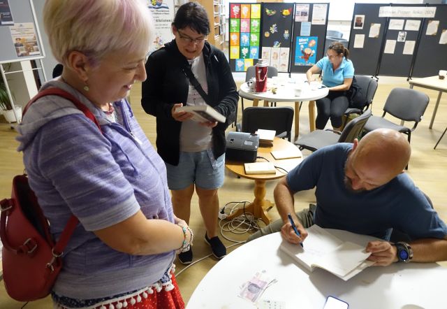 autor podpisuje książkę, obok niego stoją dwie kobiety