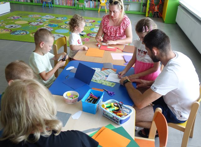 małe dzieci z opikunami przy stolikach robią laurki