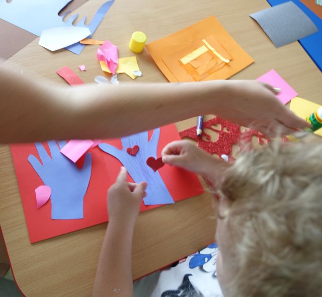 dziewczynka przykleja na wyciętych z papieru rękach serduszka