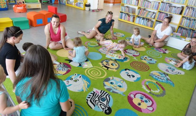 małe dzieci z mamami siedzą na kolorowym dywanie