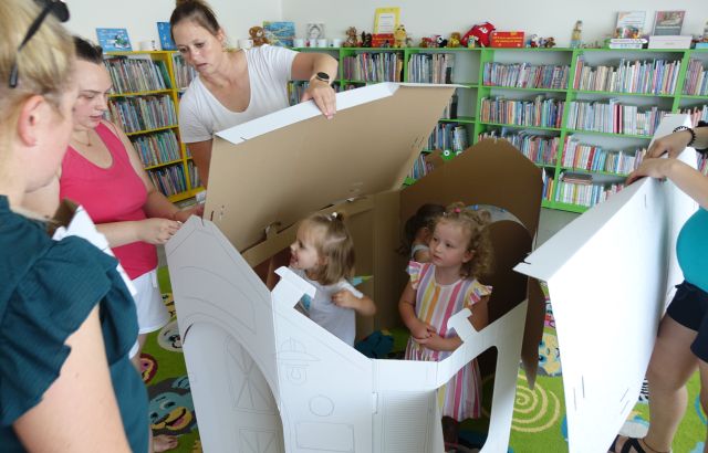 mamy składają kartonowy domek, małe dzieci chowają się w domku