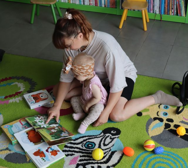 małą dziewczynka z mamą siedzący na dywanie oglądają książki