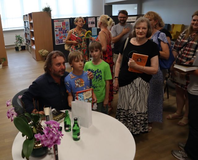 autor pozuje do zdjęcia z dwójką chłopców, w tle pozostali uczestnicy spotkania