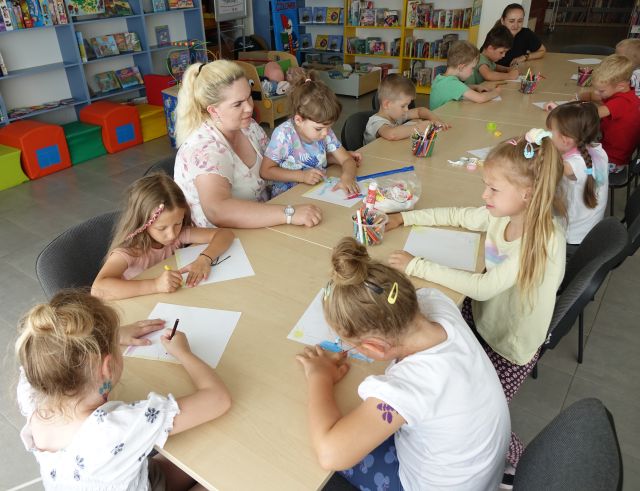 przedszkolaki siedzące przy stołach malują na kartkach