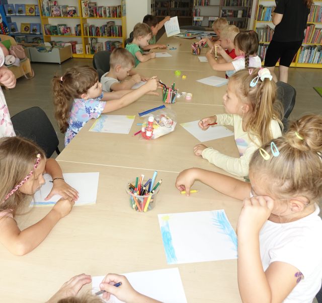 przedszkoalki siedzą przy stołach i malują na kartkach