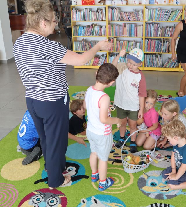 przedszkolaki siedząc na kolorowym dywanie oglądają fanty wyciągnięte z worka