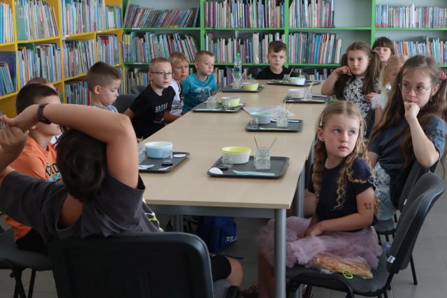 dzieci siedzą przy stołach, na stołąch tacki i szklaneczki do doświadczeń