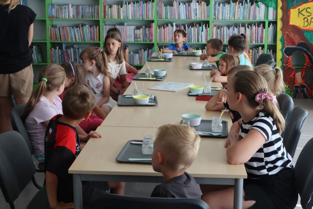 dzieci siedzą przy stołach, na stołąch tacki i szklaneczki do doświadczeń
