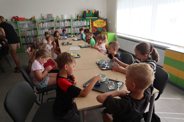 dzieci siedzące przy stołach, na stołach na tackach słoiczki z kolorowymi płynami