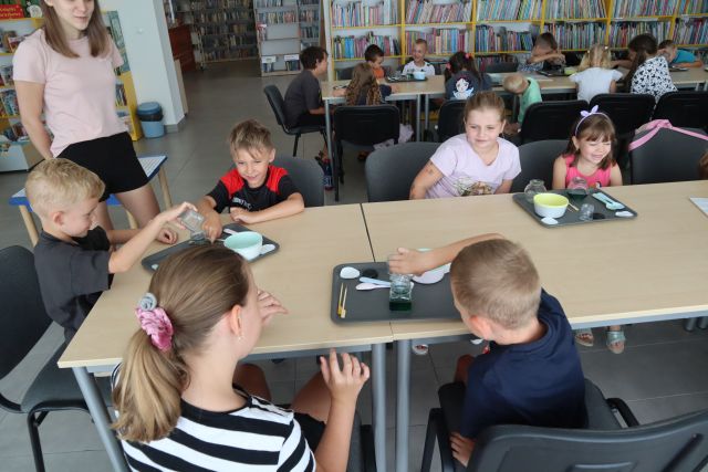 dzieci siedzące na stołach obserwują zmieniające się kolory płynów w słoiczkach