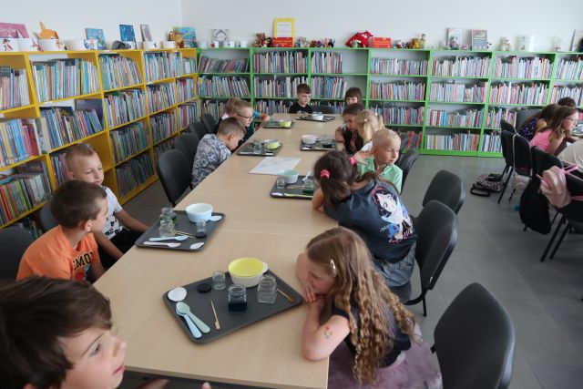 dzieci siedzące na stołach obserwują zmieniające się kolory płynów w słoiczkach