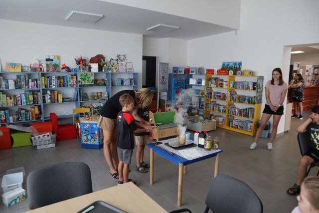 dwoje dzieci z kobietą patrzą na dym unoszący się ze słoika