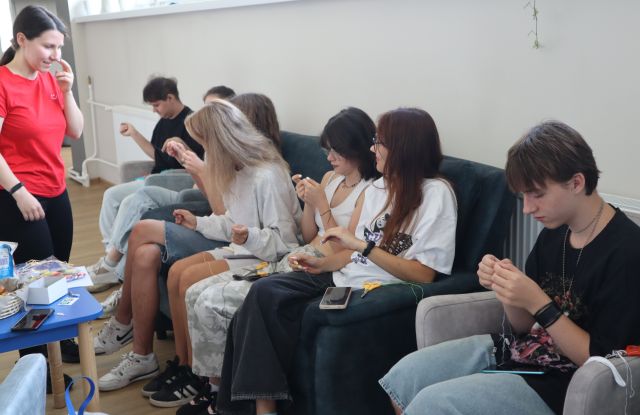 8 młodych osóbhaftuje siedząc na fotelach i sofie