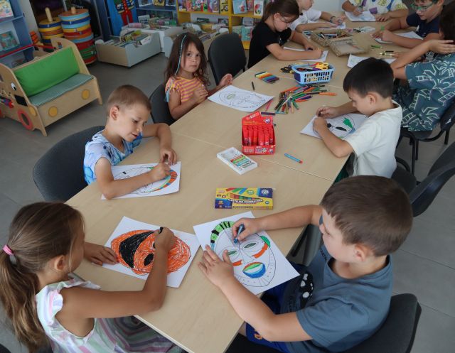przedszkolaki przy stolikach kolorują maski