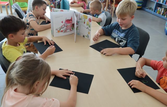 dzieci na czarnych kartkach wydrapują rysunki