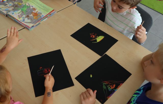 dzieci na czarnych kartkach wydrapują rysunki
