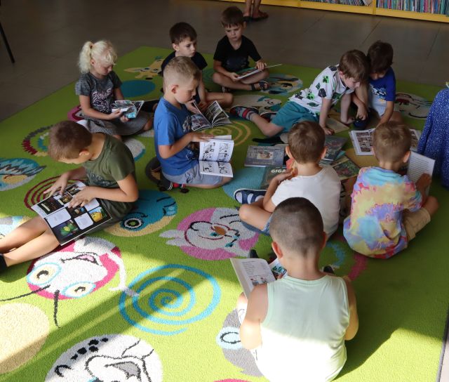 dzieci siedząc na kolorowym dywanie ogląda komiksy