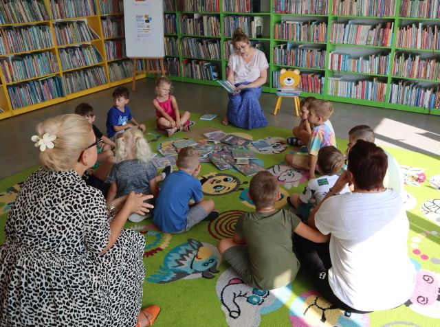 bibliotekarka siedząca na krzesełju czyta dzieciom książkę