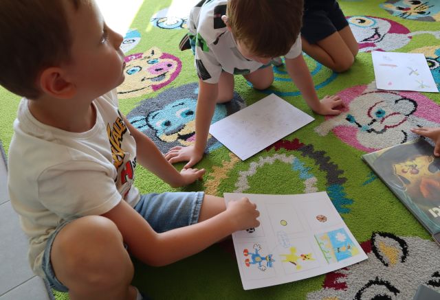 dzieci siedzące na kolorowym dywanie trzyma na kolanach swoje komiksy