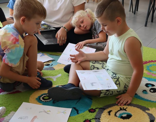 dzieci siedzą na kolorowym dywanie ze swoimi komiksami