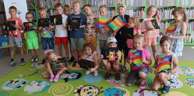 przedszkolaki pozują do zdjęcia ze swoimi ilustracjami wydrapywankami, w tle regały z książkami