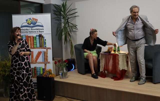 aktor stoi i zdejmuje marynarkę, prowadząca spotaknie siedzi i nalewa do literatki wodę, dyrektorka mówi do mikrofonu