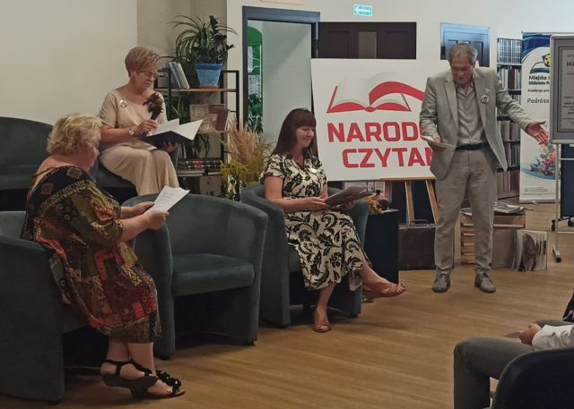 dwie kobiety i aktor czytający tekst lektury, obok baner z Narodowym Czytaniem
