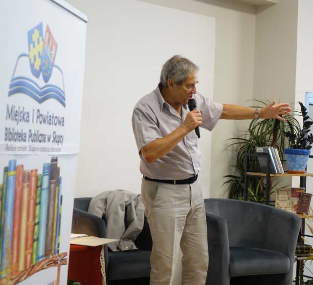 aktor stoi i mówi do mikrofonu pokazując ręką w prawą stronę