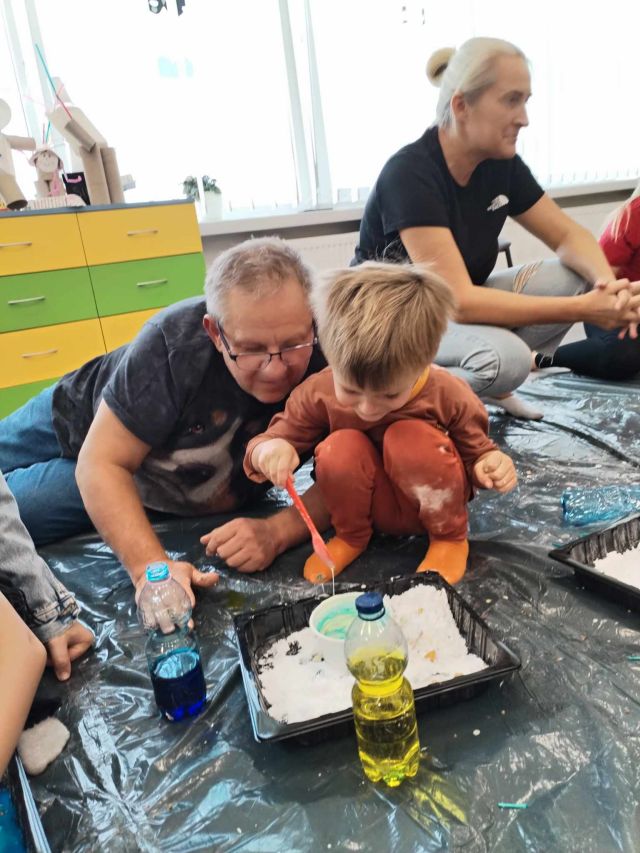 chłopiec z dziadkiem miesza kolorowy płyn z różnymi masami tworząc lepką maź