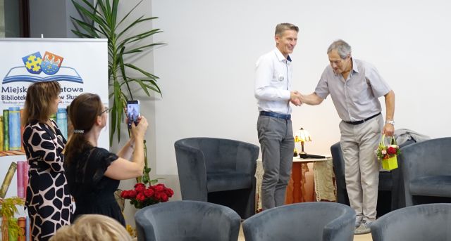 burmistrz dziękuje aktorowi i wręcza mu kwiaty, przy scenie stoi dyrektorka biblioteki z kobietą z aparatem