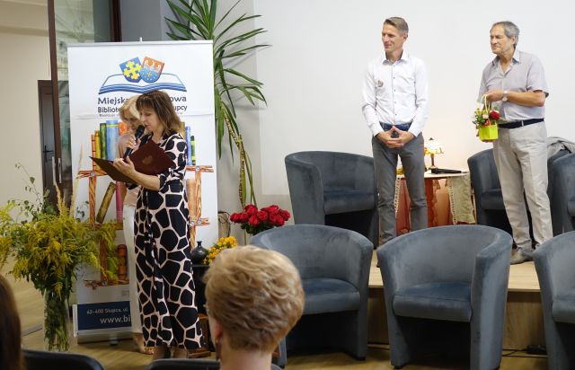 na scenie stoi burmistrz i aktor, przed sceną dyrektorka biblioteki wręcza dziewczynie i chłopakowi prezenty