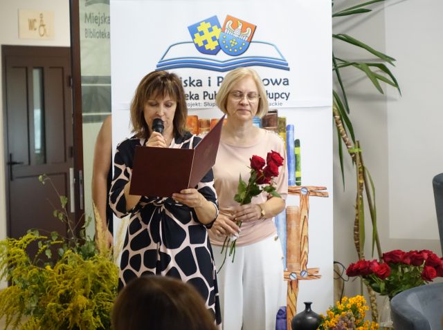 dyrektorka biblioteki czyta pożegnanie, obok stoi bibliotekarka z kwiatami