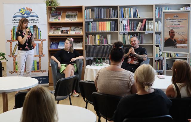 na zdjęciu uczestnicy spotkania z autorem Orbitowski, w tle regały z książkami