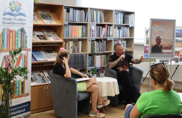 na zdjęciu autor książek i prowadząca spotkanie, w tle regały z książkami