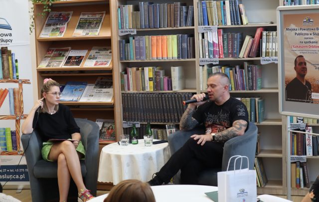 na zdjęciu autor książek i prowadząca spotkanie, w tle regały z książkami