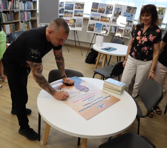 autor podpisujący się na plakacie, obok dyrektorka biblioteki