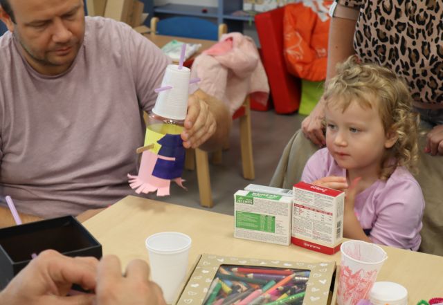 tata pokazuje robota z materiałów recyklingowych, obok siedzi dziewczynka