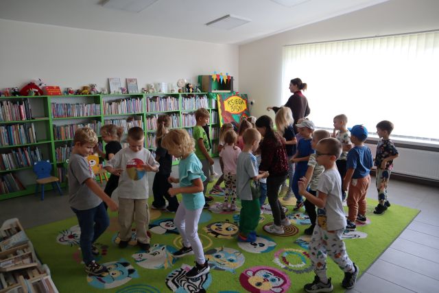 dzieci bawią się chodząc po kolorowym dywanie, w tle regały z książkami