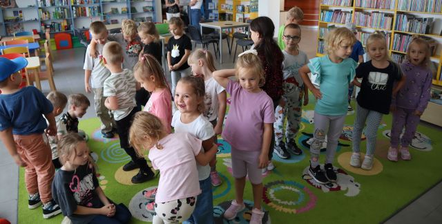 dzieci bawią się chodząc po kolorowym dywanie, w tle regały z książkami