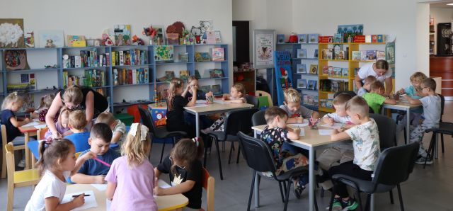 dzieci siedzą przy stolikach, w tle regały z książkami