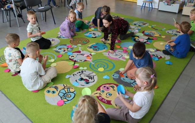 dzieci na kolorowym dywanie zbierają kolorowe okrągłe karteczki