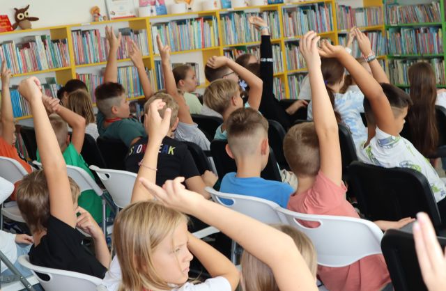 dzieci siedzą i podnoszą do góry ręce chcąc o coś zapytać