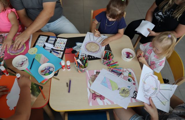 uczestniczący w warsztatach rodzice i dzieci wykonują przy stoliku ordery uśmiechu