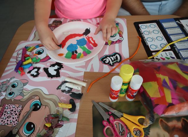 na zdjęciu dłonie dziecka wyklejające plasteliną na papierowym talerzyku uśmiechniętą twarz