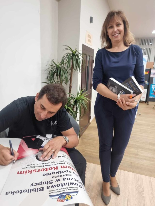 dyrektorka biblioteki stojąca obok aktora podpisującego książki