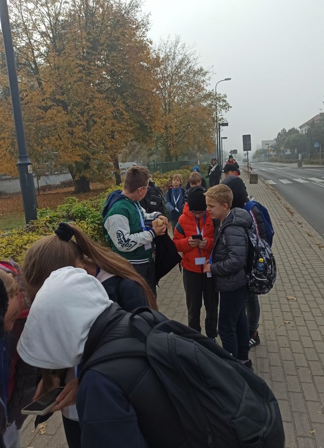 młodzież spaceruje po mieście ze smartfonami rozwiązując zadania gry mobilnej