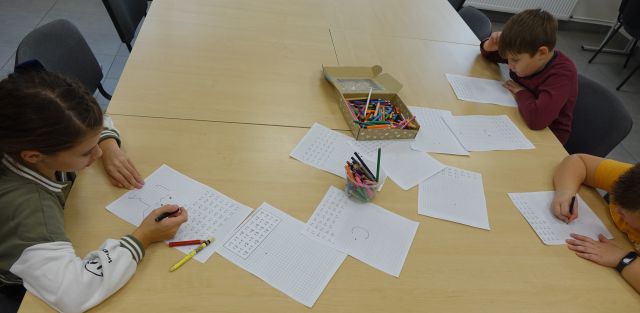 3 dzieci pisze na kartkach