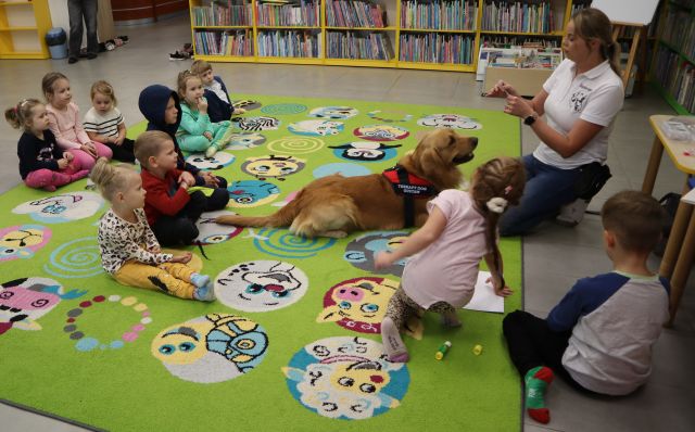 dzieci siedzą z psem na kolorowym dywanie, w tle regały z książkami