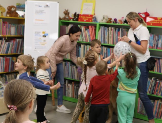 dzieci w grupce czekają na nadmuchanie balonów przez terapeutkę, w tle regały z książkami